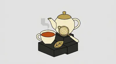 A cream teapot and a cup of steaming tea rest on dark blocks alongside a gold tea strainer and a single leaf.