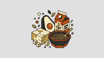 A halved avocado, a carton with a leafy sprig on it, a block of tofu with small cubes, and a bowl of lentils with a spoon.